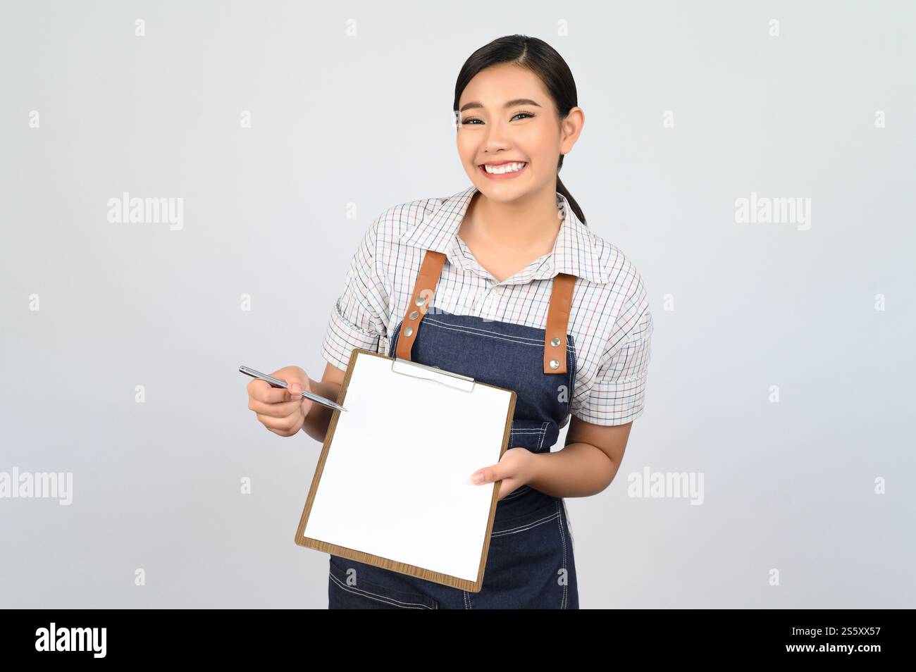 Portrait de jeune femme asiatique en uniforme de serveuse tenant maquette de presse-papiers avec stylo, espace de copie pour insérer du texte pour la publicité isolé sur blanc Banque D'Images