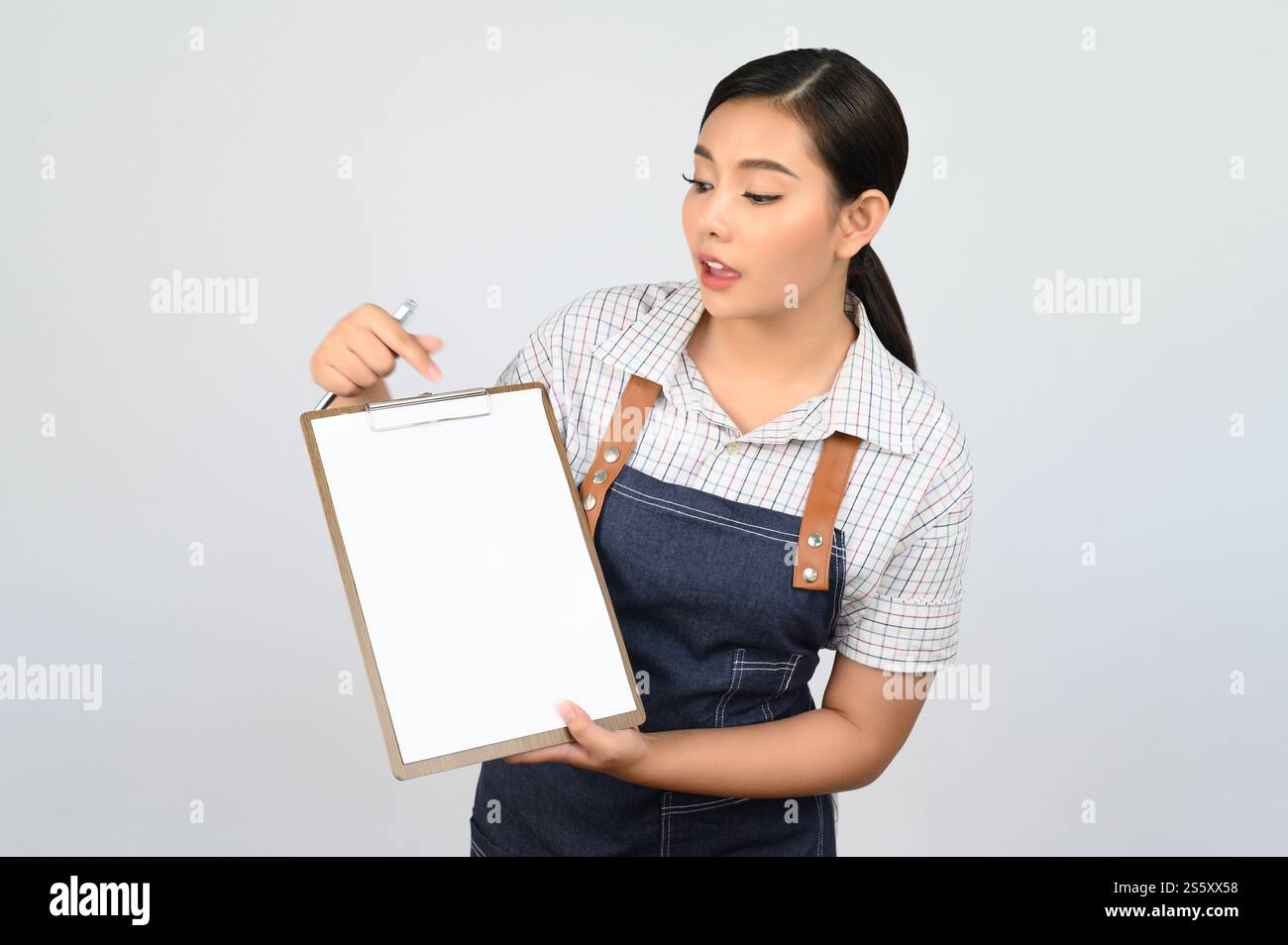 Portrait de jeune femme asiatique en uniforme de serveuse tenant maquette de presse-papiers avec stylo, espace de copie pour insérer du texte pour la publicité isolé sur blanc Banque D'Images