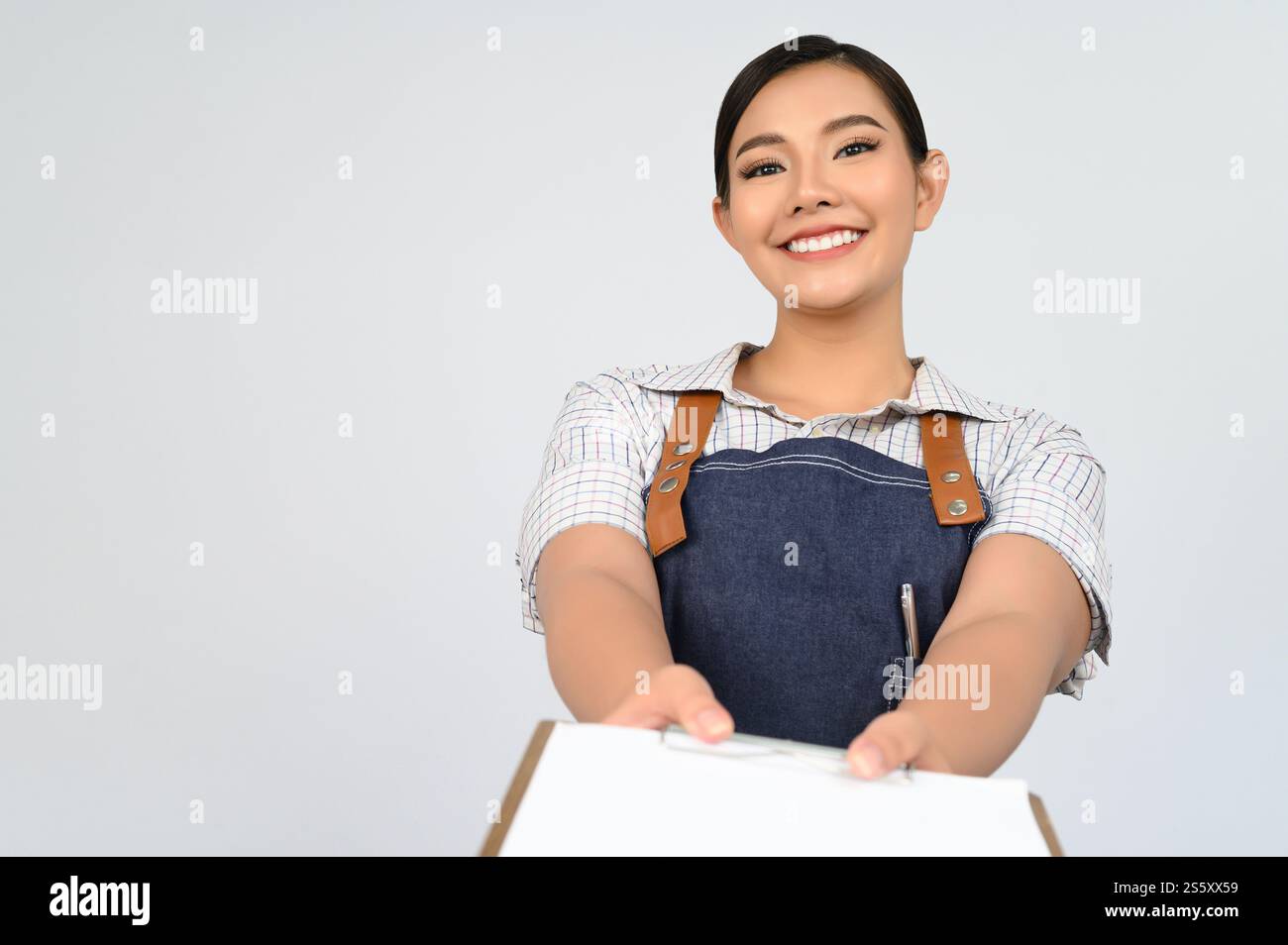 Portrait de jeune femme asiatique en uniforme de serveuse tenant maquette de presse-papiers avec stylo, espace de copie pour insérer du texte pour la publicité isolé sur blanc Banque D'Images