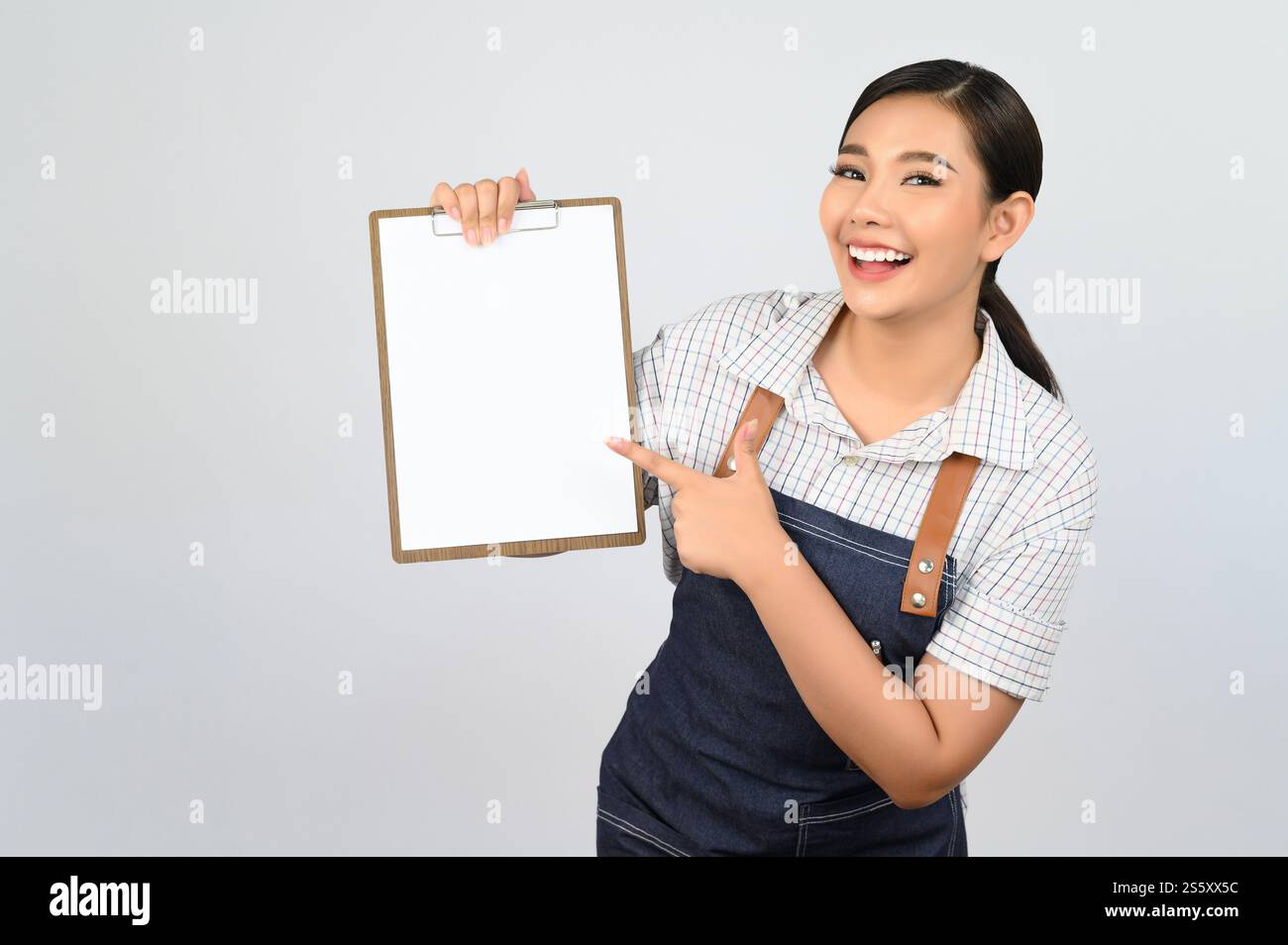 Portrait de jeune femme asiatique en uniforme de serveuse tenant maquette de presse-papiers avec stylo, espace de copie pour insérer du texte pour la publicité isolé sur blanc Banque D'Images