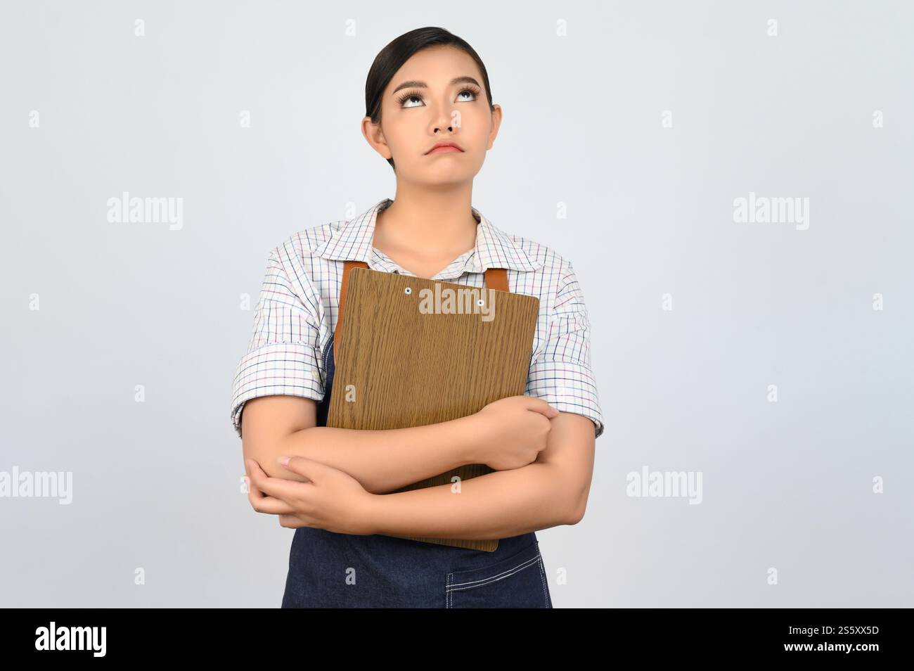 Portrait de jeune femme asiatique dans l'uniforme de serveuse tenant le presse-papiers sur la poitrine et regardant vers le haut avec bouleversement, espace de copie pour insérer des produits pour Banque D'Images