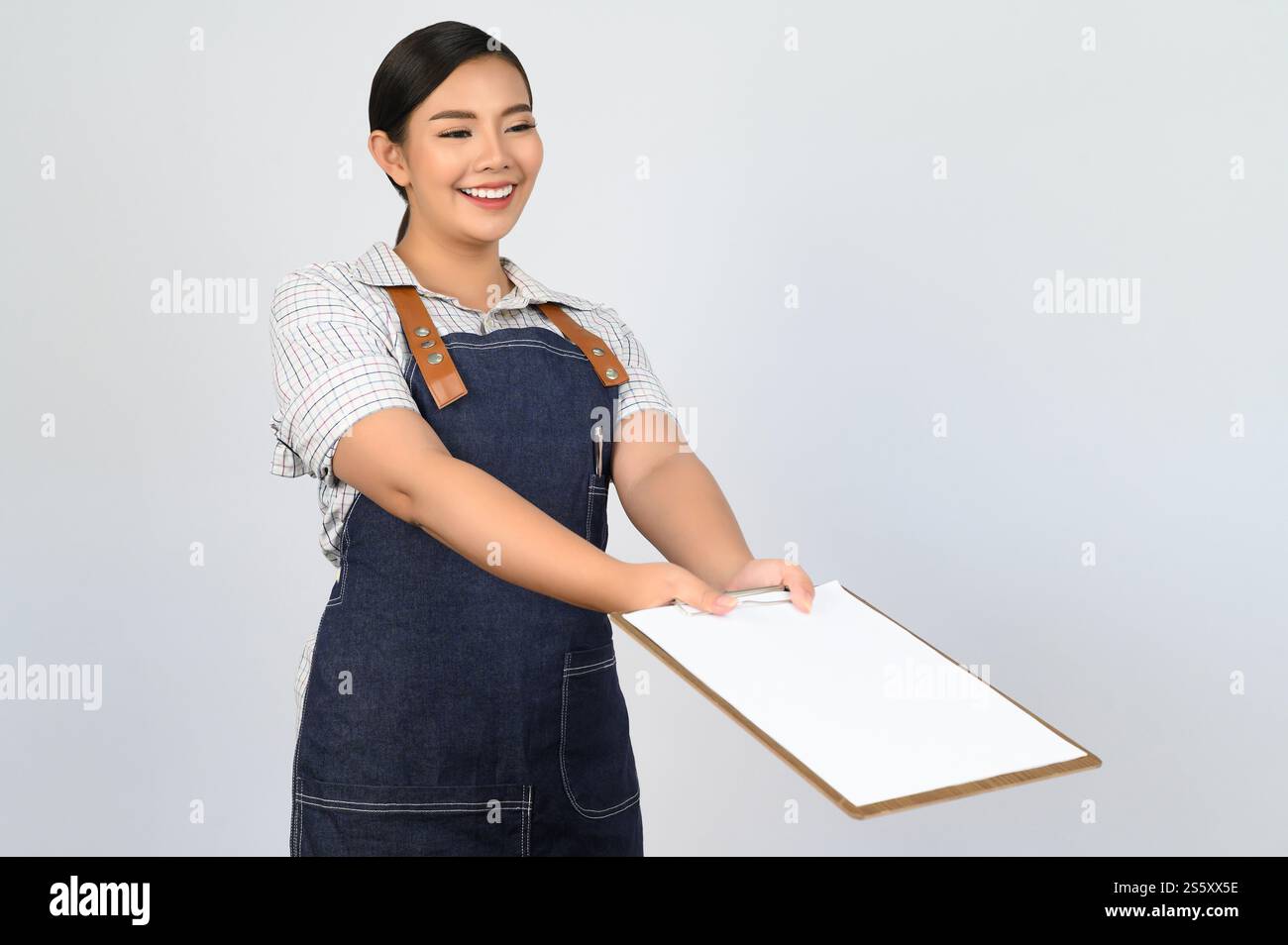 Portrait de jeune femme asiatique en uniforme de serveuse tenant maquette de presse-papiers avec stylo, espace de copie pour insérer du texte pour la publicité isolé sur blanc Banque D'Images