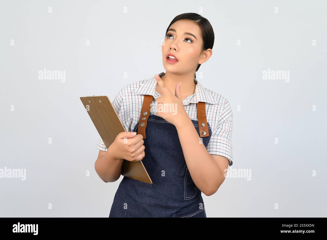 Portrait de jeune femme asiatique dans l'uniforme de serveuse tenant le presse-papiers et le doigt de pointe, copiez l'espace pour insérer des produits pour la publicité isolé sur Banque D'Images