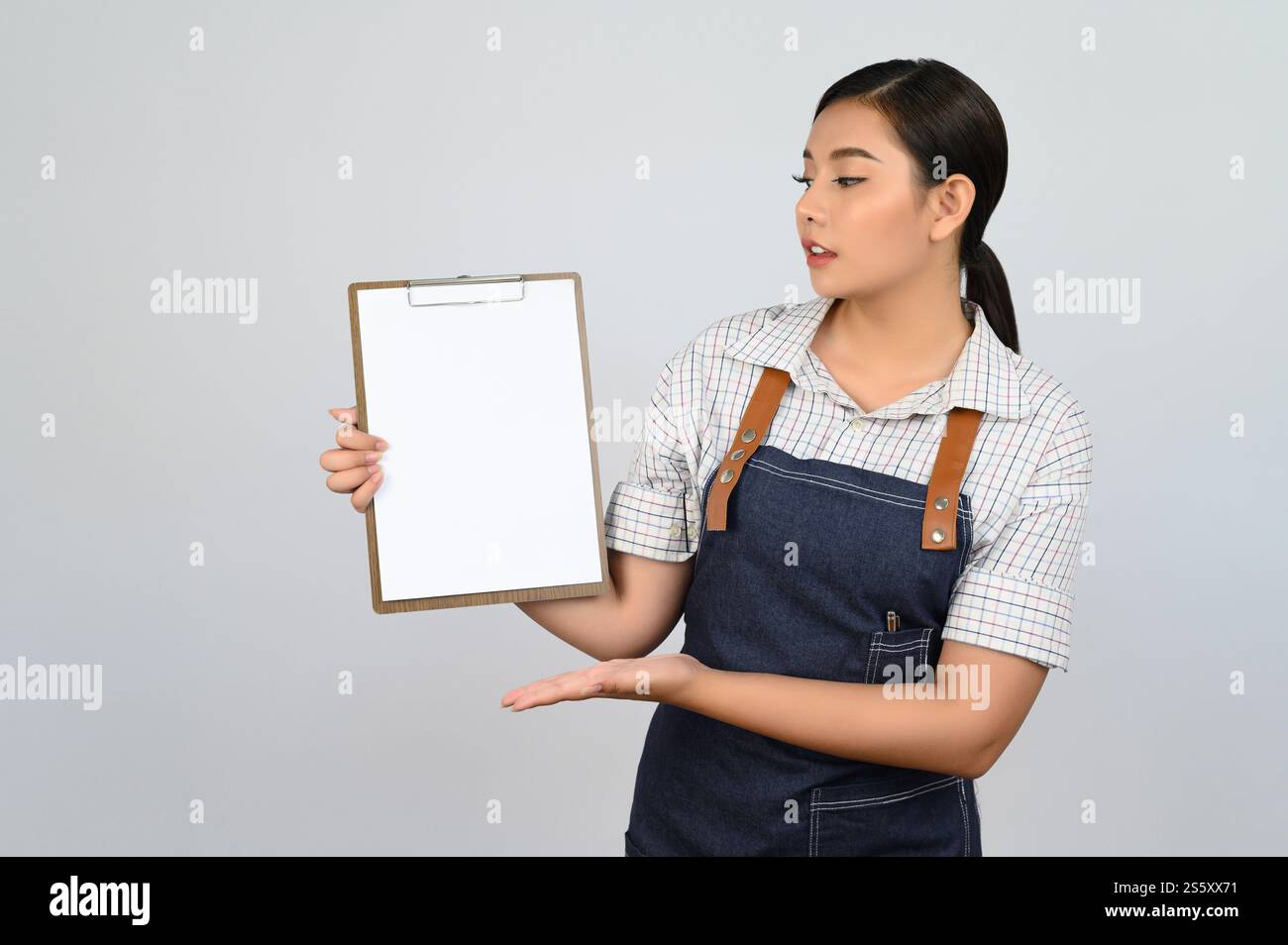 Portrait de jeune femme asiatique en uniforme de serveuse montrant maquette de presse-papiers à la main avec sourire, espace de copie pour insérer du texte pour la publicité isolé Banque D'Images
