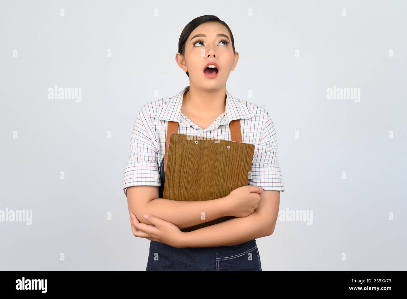 Portrait de jeune femme asiatique dans l'uniforme de serveuse tenant le presse-papiers et regardant vers le haut, copiez l'espace pour insérer des produits pour la publicité isolé sur blanc Banque D'Images