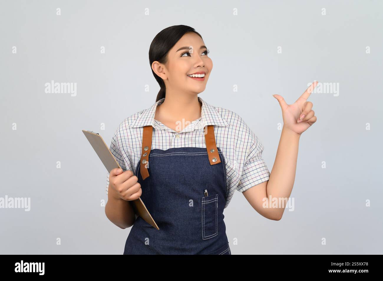 Portrait de jeune femme asiatique dans l'uniforme de serveuse tenant le presse-papiers et le doigt de pointe, copiez l'espace pour insérer des produits pour la publicité isolé sur Banque D'Images