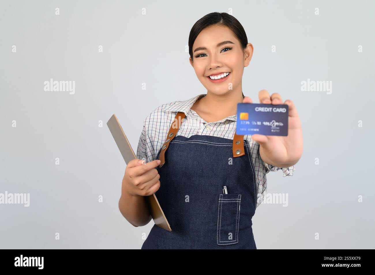 Focus sélectif, jeune femme asiatique en uniforme de serveuse pose avec carte de crédit à la main, espace de copie pour insérer des produits pour la publicité isolé sur Banque D'Images