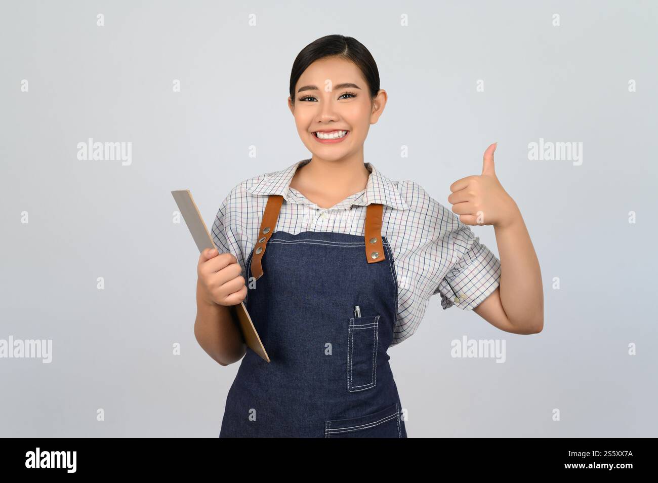 Portrait de jeune femme asiatique dans l'uniforme de serveuse tenant presse-papiers et pouce vers le haut pose, copiez l'espace pour insérer des produits pour la publicité isolé sur Banque D'Images