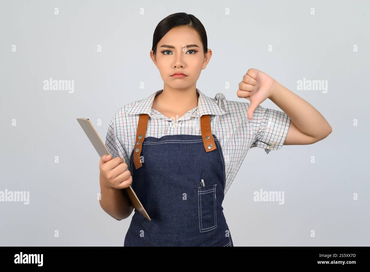 Portrait de jeune femme asiatique en uniforme de serveuse tenant le presse-papiers et le pouce vers le bas avec la pose bouleversée, espace de copie pour insérer des produits pour la publicité Banque D'Images