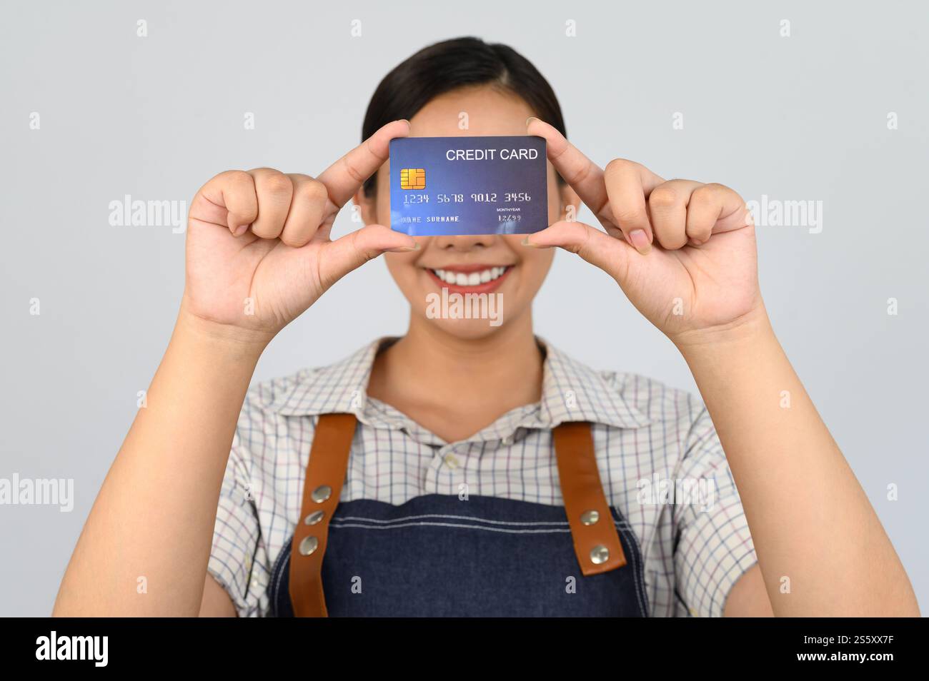 Portrait de jeune femme asiatique dans la pose uniforme de serveuse montrant la carte de crédit en main, espace de copie pour insérer des produits pour la publicité isolé sur blanc Banque D'Images
