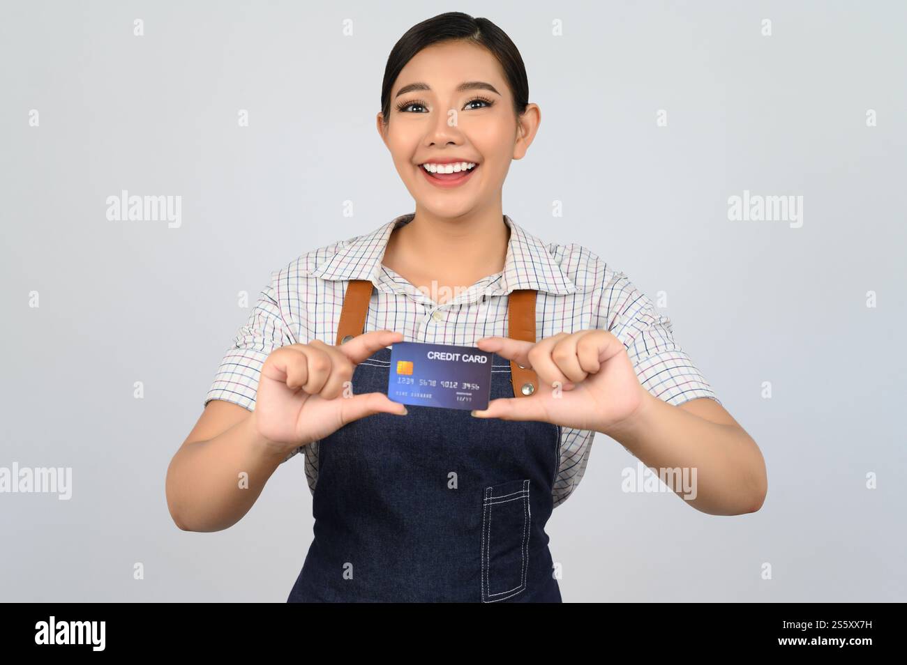 Portrait de jeune femme asiatique dans la pose uniforme de serveuse avec la carte de crédit à la main, copier l'espace pour insérer des produits pour la publicité isolé sur blanc Banque D'Images