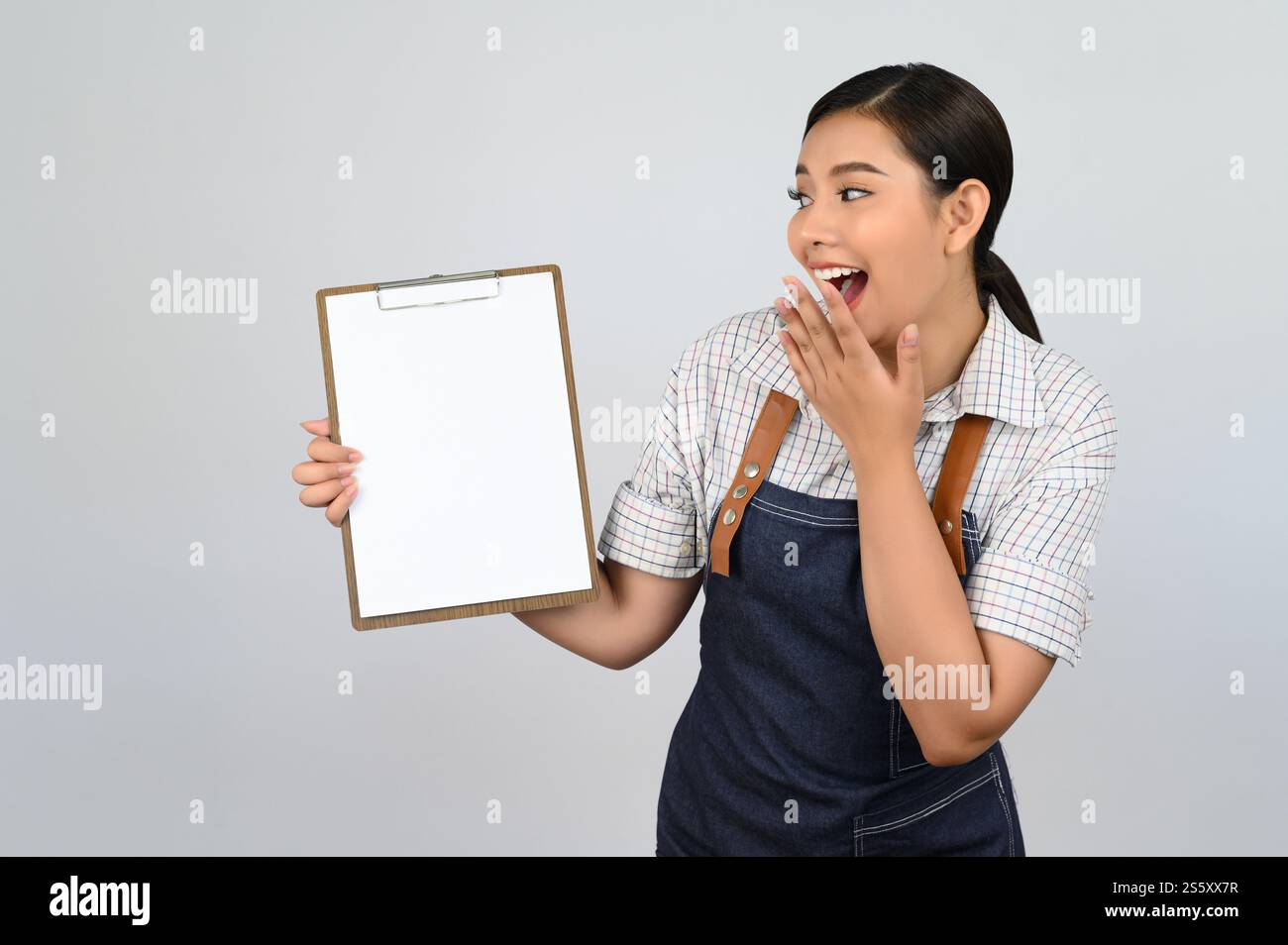 Portrait de jeune femme asiatique en uniforme de serveuse montrant maquette de presse-papiers à la main avec sourire, espace de copie pour insérer du texte pour la publicité isolé Banque D'Images