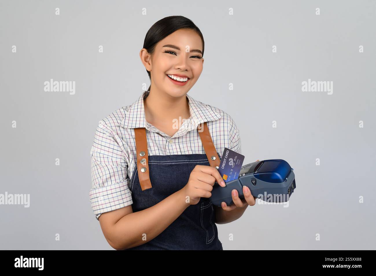 Portrait de jeune femme asiatique dans la pose uniforme de serveuse avec carte de crédit et lecteur de carte de crédit machine à la main, espace de copie pour insérer des produits pour Banque D'Images