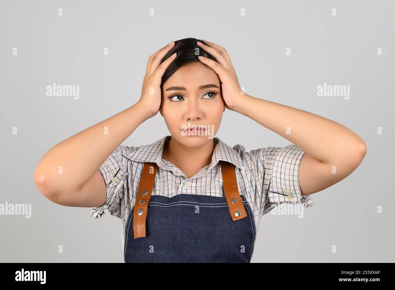 Portrait de jeune femme asiatique en uniforme de serveuse avec posture de mal de tête, elle soulève la tête de couverture de deux mains avec stressant avec le travail fatigué, isolé sur Banque D'Images