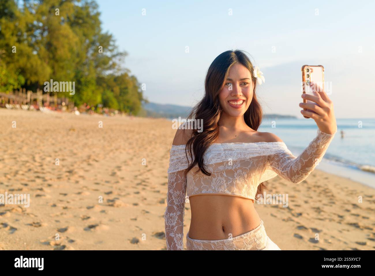 Femme asiatique appel vidéo sur le téléphone par la plage au concept Golden Hour Banque D'Images