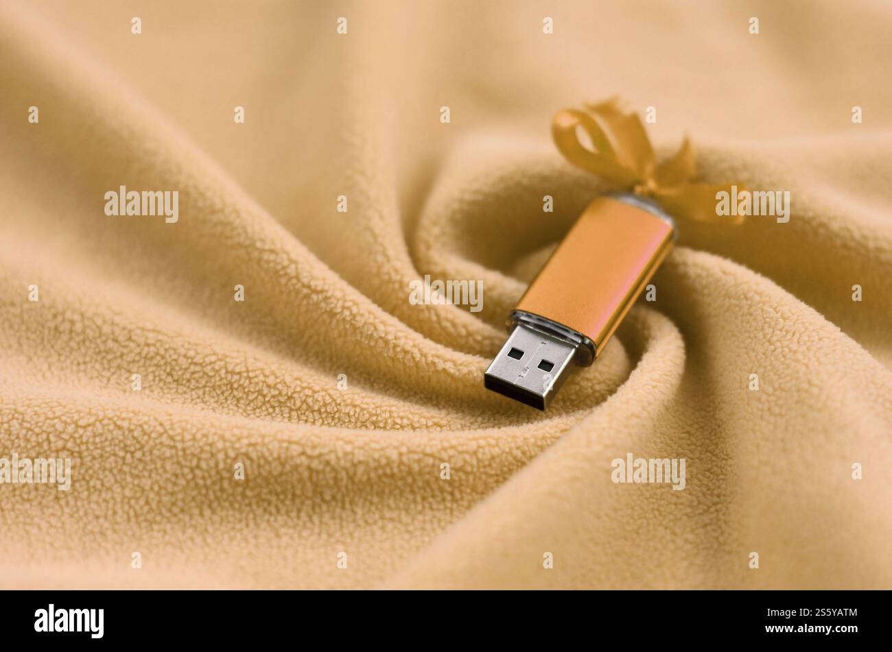 La carte mémoire flash usb orange avec un noeud repose sur une couverture de tissu polaire orange clair doux et fourré avec beaucoup de plis en relief. Stockage en mémoire Banque D'Images
