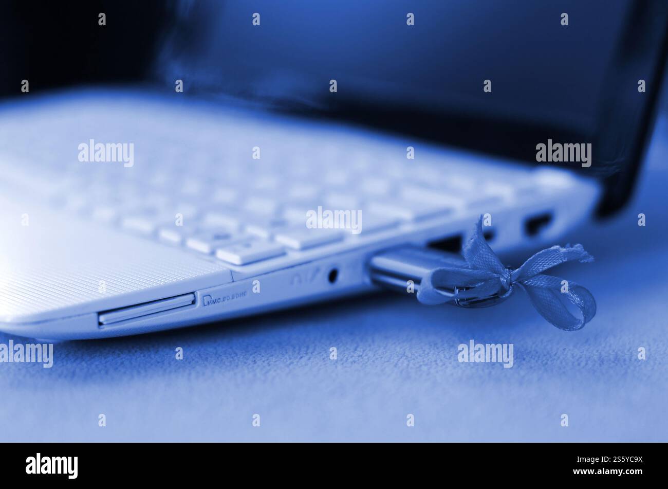 Le lecteur flash USB avec arc est connecté à un ordinateur portable blanc, qui repose sur une couverture de tissu polaire doux et moelleux. fantôme de couleur bleue classique. A Banque D'Images