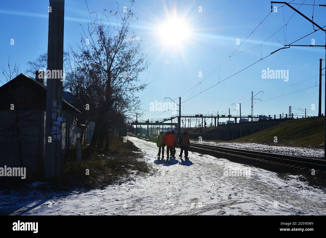 Plusieurs cheminots en signalant des uniformes orange sales sont sur la route à côté de la ligne de chemin de fer. L'équipe du train se rend au travail en hiver ensoleillé Banque D'Images