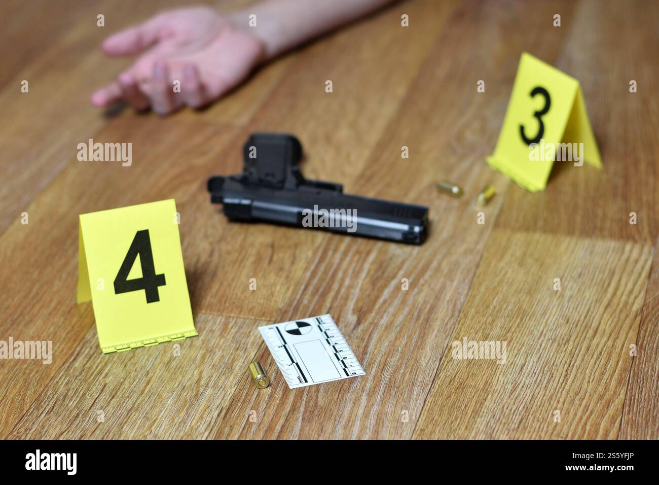 Main de jeune homme et arme à feu avec des obus sur plancher en bois. Concept de suicide commis, marqueurs d'enquête sur la scène de crime en gros plan. Main de jeune homme Banque D'Images
