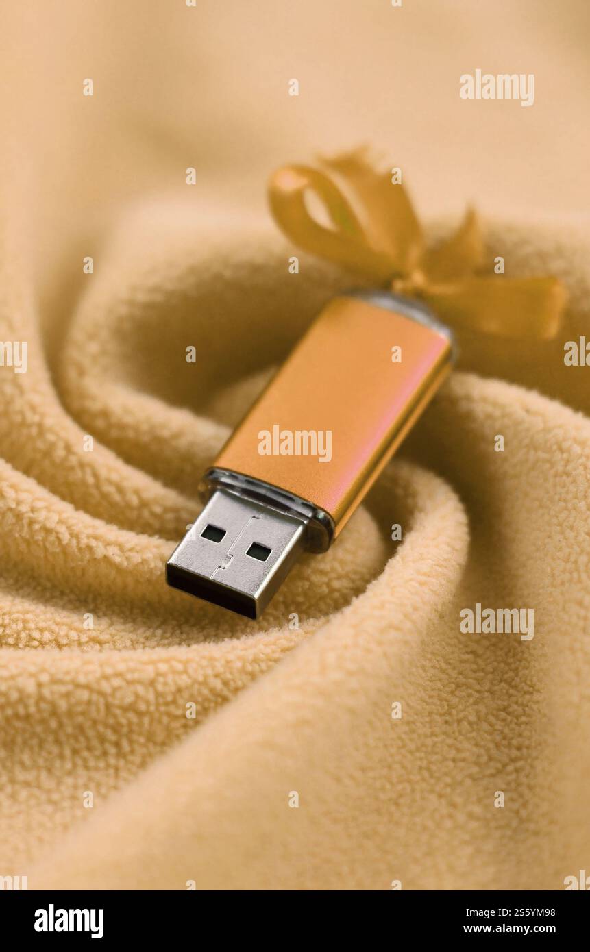 La carte mémoire flash usb orange avec un noeud repose sur une couverture de tissu polaire orange clair doux et fourré avec beaucoup de plis en relief. Stockage en mémoire Banque D'Images