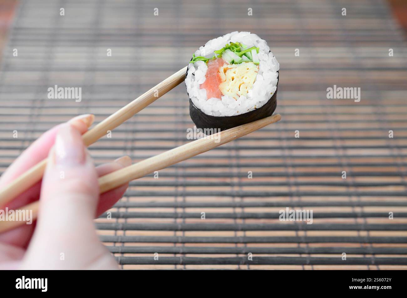 Une main avec des baguettes tient un rouleau de sushi sur un fond de tapis de serwing en paille de bambou. Cuisine asiatique traditionnelle. Une main avec des baguettes tient un rouleau de sushi Banque D'Images
