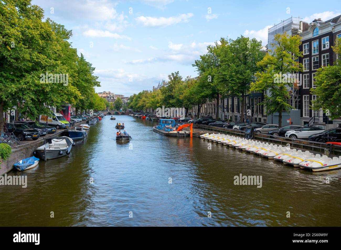 Image éditoriale d'une scène animée de canal à Amsterdam avec un groupe de personnes profitant d'une promenade en bateau sous un ciel bleu clair, mettant en valeur la ville animée Banque D'Images