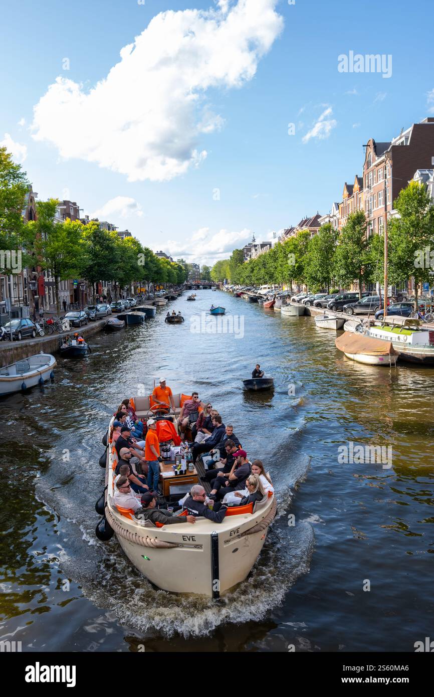 Image éditoriale d'une scène animée de canal à Amsterdam avec un groupe de personnes profitant d'une promenade en bateau sous un ciel bleu clair, mettant en valeur la ville animée Banque D'Images