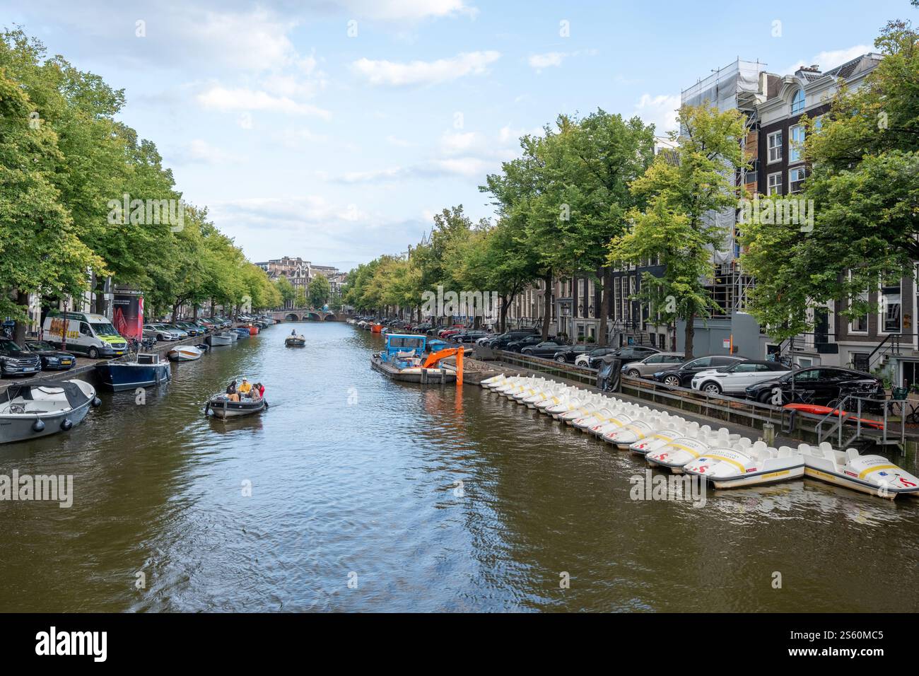 Image éditoriale d'une scène animée de canal à Amsterdam avec un groupe de personnes profitant d'une promenade en bateau sous un ciel bleu clair, mettant en valeur la ville animée Banque D'Images