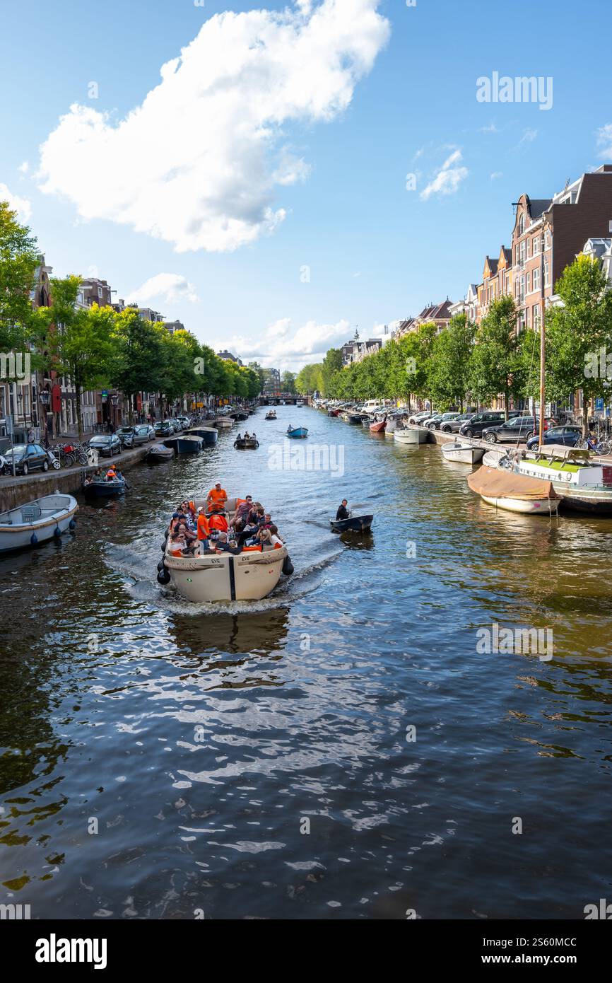 Image éditoriale d'une scène animée de canal à Amsterdam avec un groupe de personnes profitant d'une promenade en bateau sous un ciel bleu clair, mettant en valeur la ville animée Banque D'Images