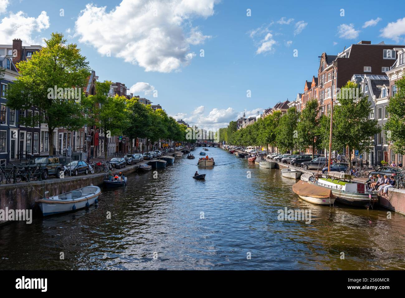 Image éditoriale d'une scène animée de canal à Amsterdam avec un groupe de personnes profitant d'une promenade en bateau sous un ciel bleu clair, mettant en valeur la ville animée Banque D'Images
