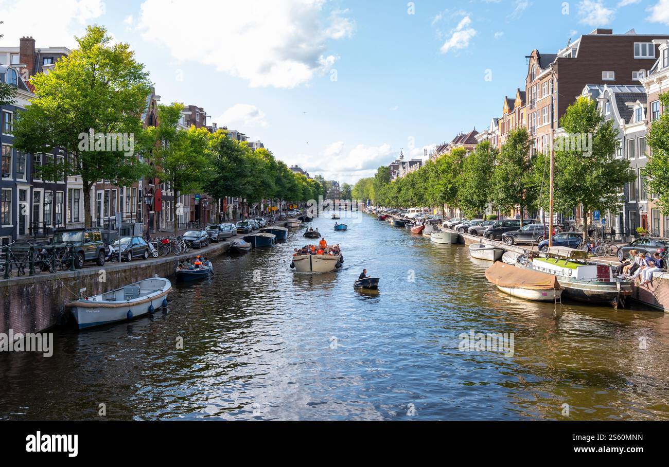 Image éditoriale d'une scène animée de canal à Amsterdam avec un groupe de personnes profitant d'une promenade en bateau sous un ciel bleu clair, mettant en valeur la ville animée Banque D'Images