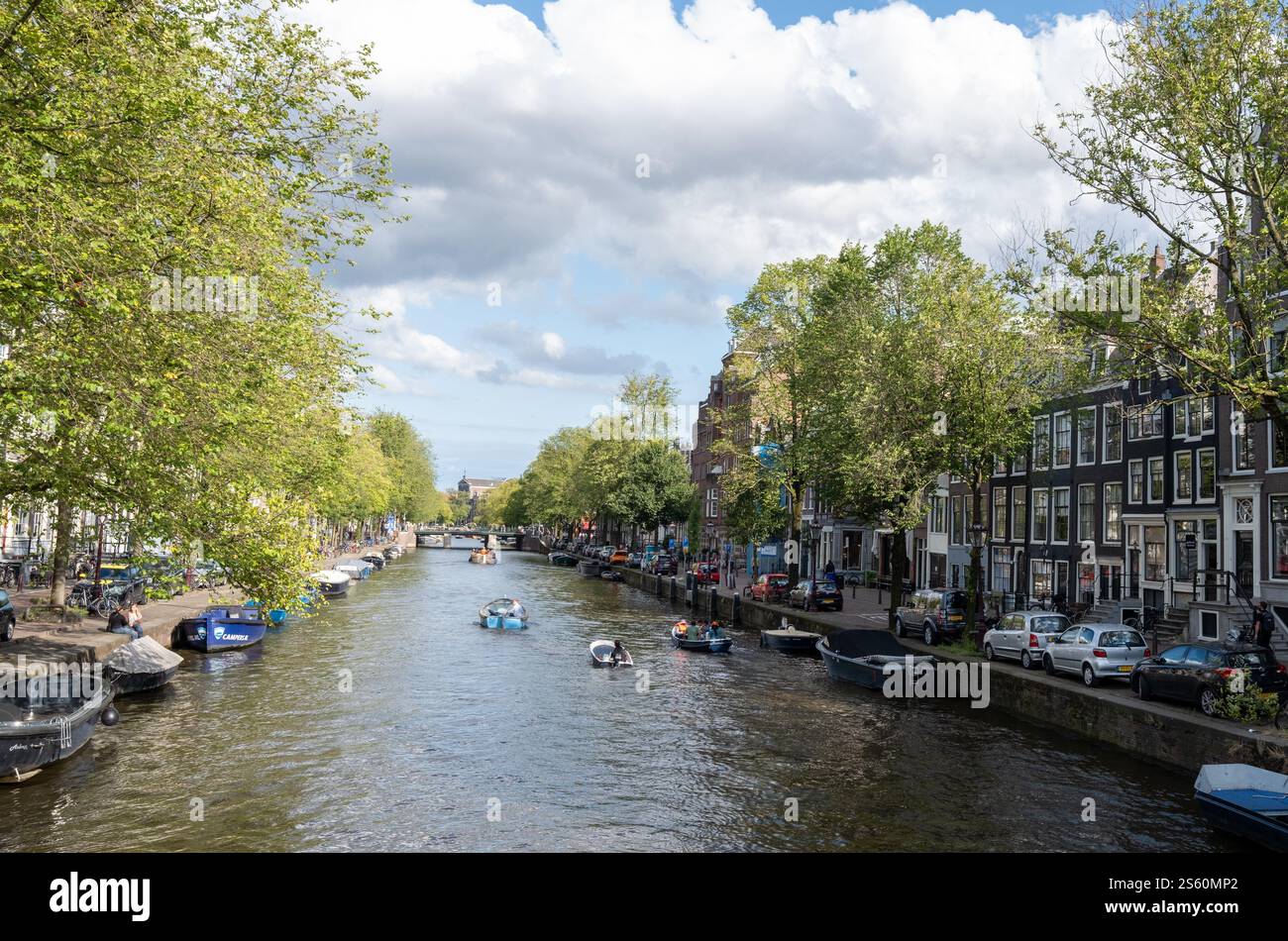 Image éditoriale d'une scène animée de canal à Amsterdam avec un groupe de personnes profitant d'une promenade en bateau sous un ciel bleu clair, mettant en valeur la ville animée Banque D'Images