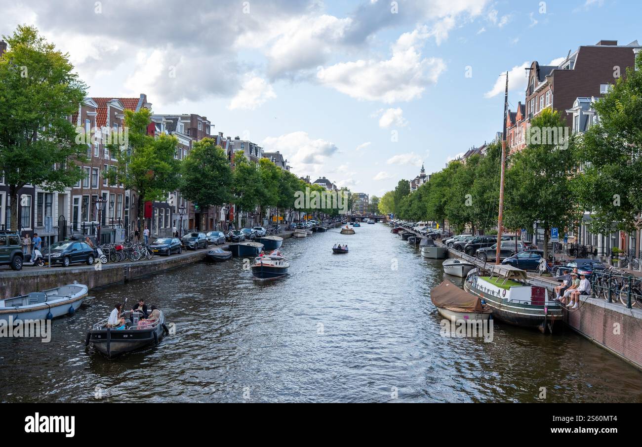 Image éditoriale d'une scène animée de canal à Amsterdam avec un groupe de personnes profitant d'une promenade en bateau sous un ciel bleu clair, mettant en valeur la ville animée Banque D'Images