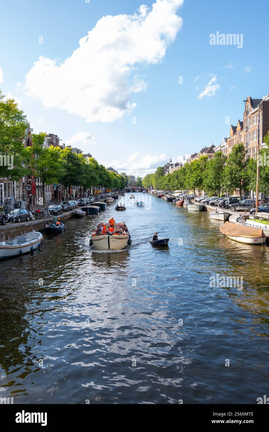 Image éditoriale d'une scène animée de canal à Amsterdam avec un groupe de personnes profitant d'une promenade en bateau sous un ciel bleu clair, mettant en valeur la ville animée Banque D'Images