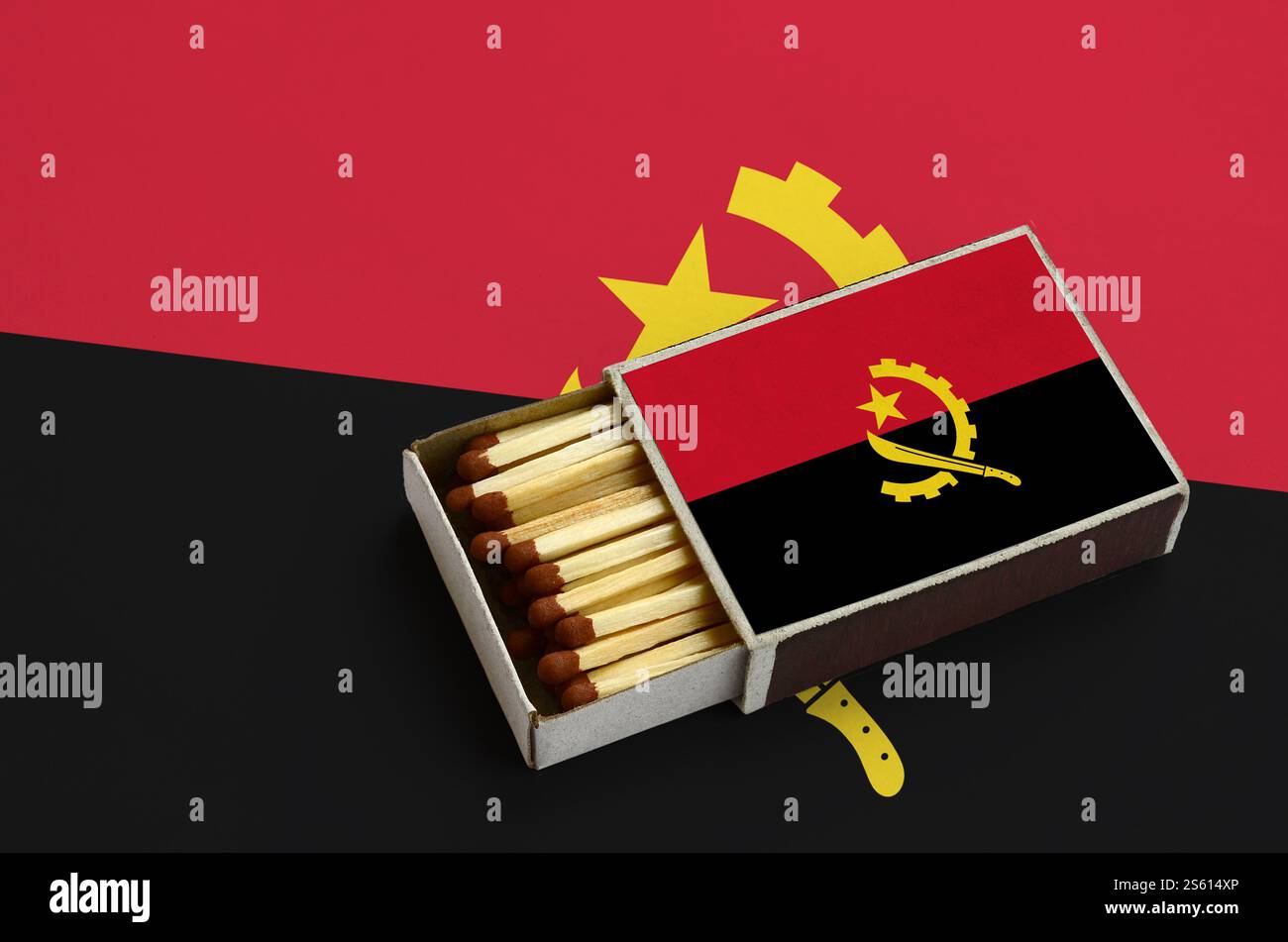 Le drapeau de l'Angola est montré dans une boîte d'allumettes ouverte, qui est remplie d'allumettes et repose sur un grand drapeau. Le drapeau de l'Angola est affiché dans une boîte d'allumettes ouverte, qui est Banque D'Images