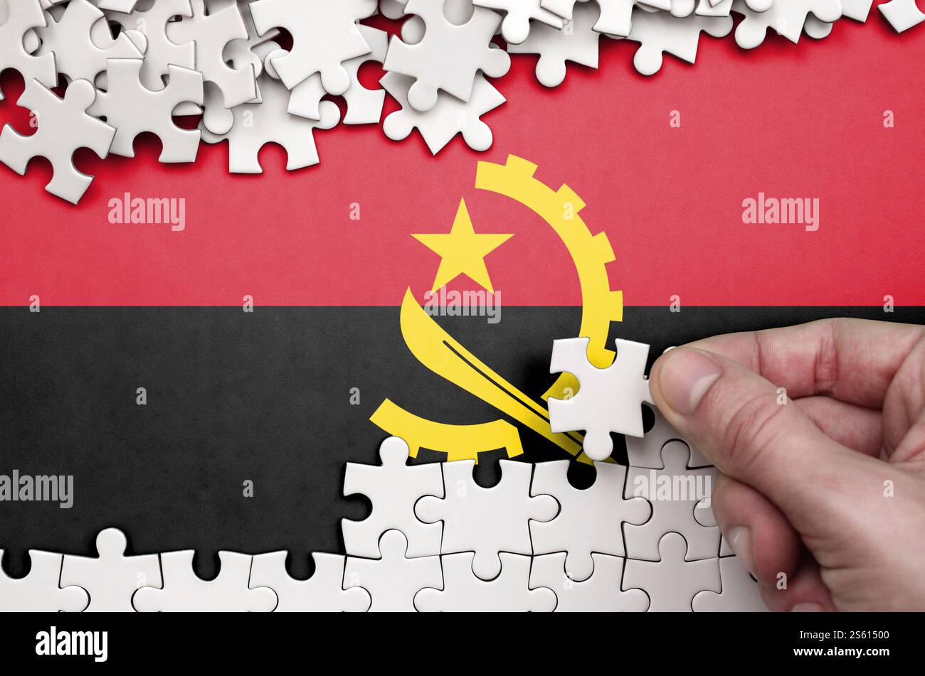Le drapeau de l'Angola est représenté sur une table sur laquelle la main humaine plie un puzzle de couleur blanche. Drapeau de l'Angola est représenté sur une table sur laquelle la main humaine Banque D'Images