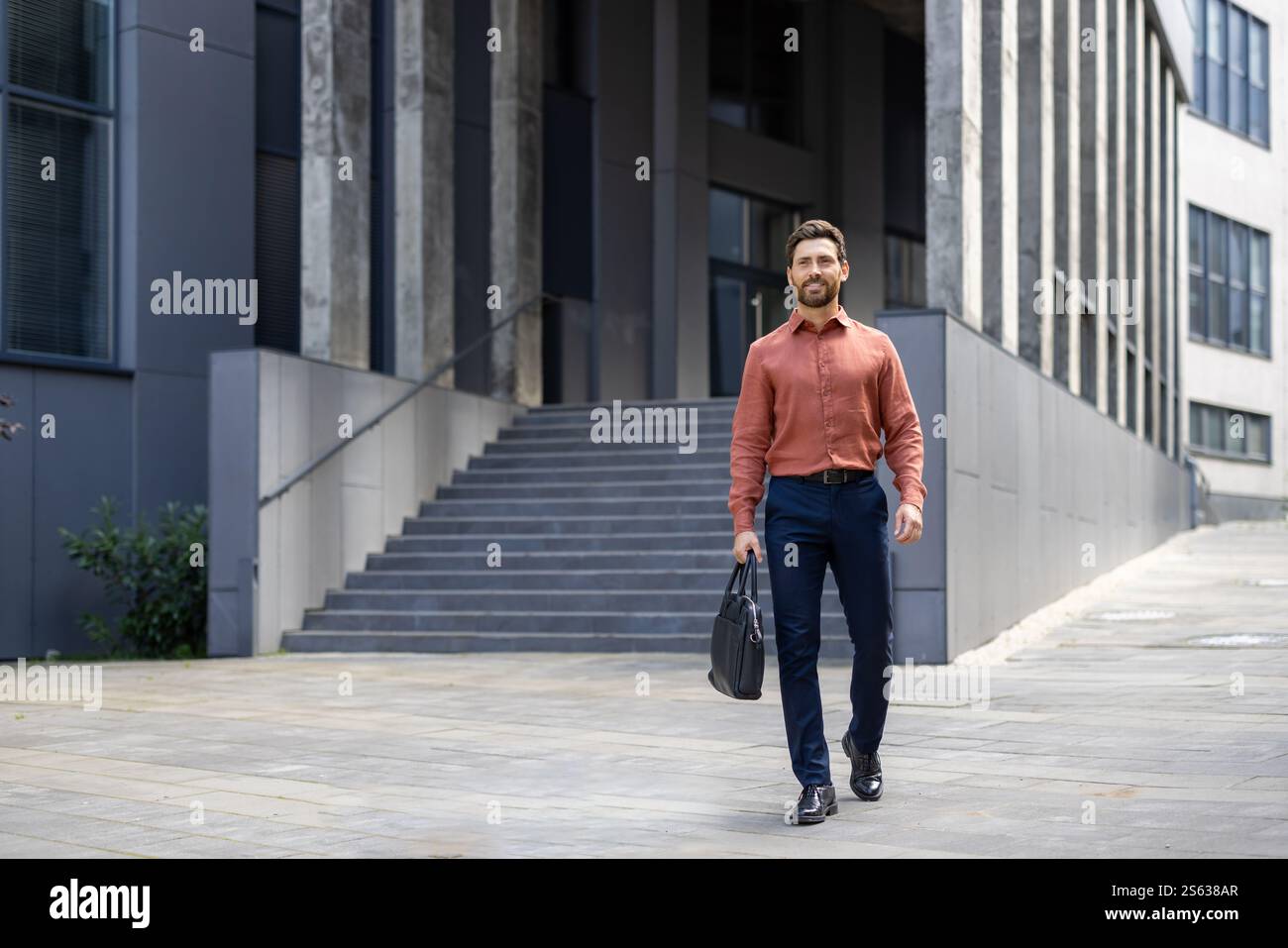 Un homme d'affaires prospère en pleine croissance se promène dans la ville avec un sac d'affaires dans ses mains, un homme mature sourit avec satisfaction de l'extérieur d'un immeuble de bureaux. Banque D'Images