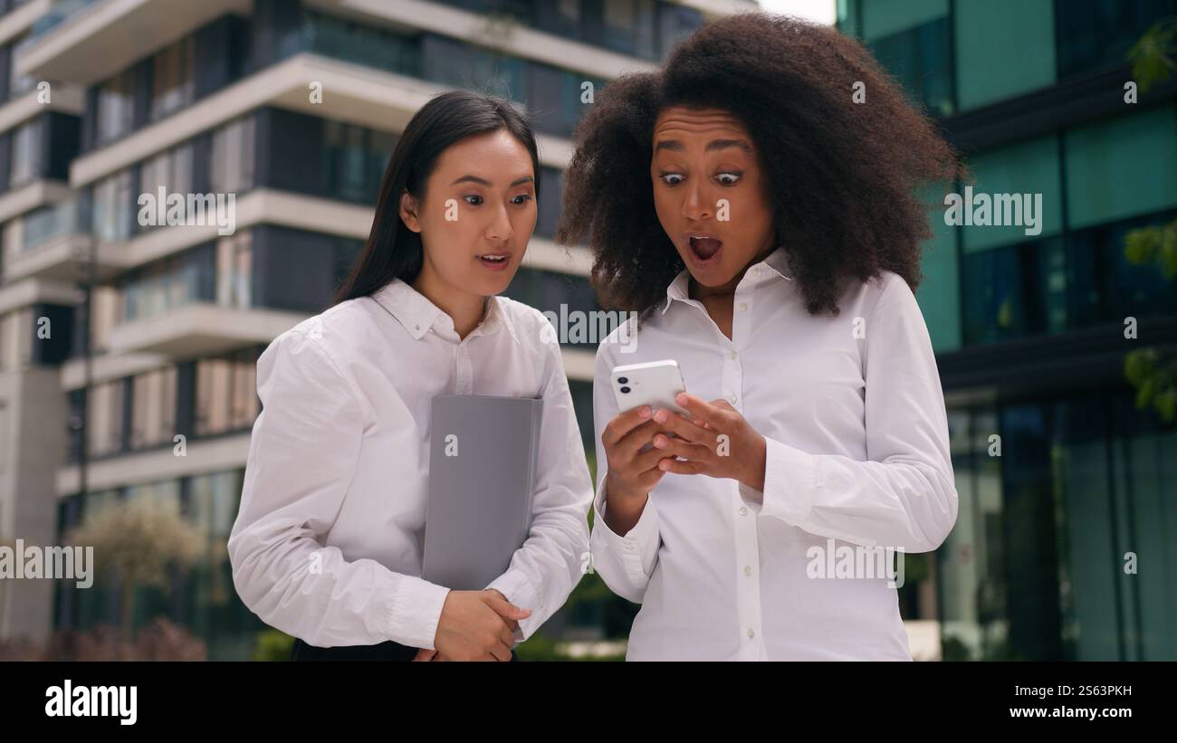 Choqué heureux afro-américain asiatique coréen femmes d'affaires collègues collègues à la recherche de téléphone mobile d'affaires smartphone bonne nouvelle excité victoire Banque D'Images