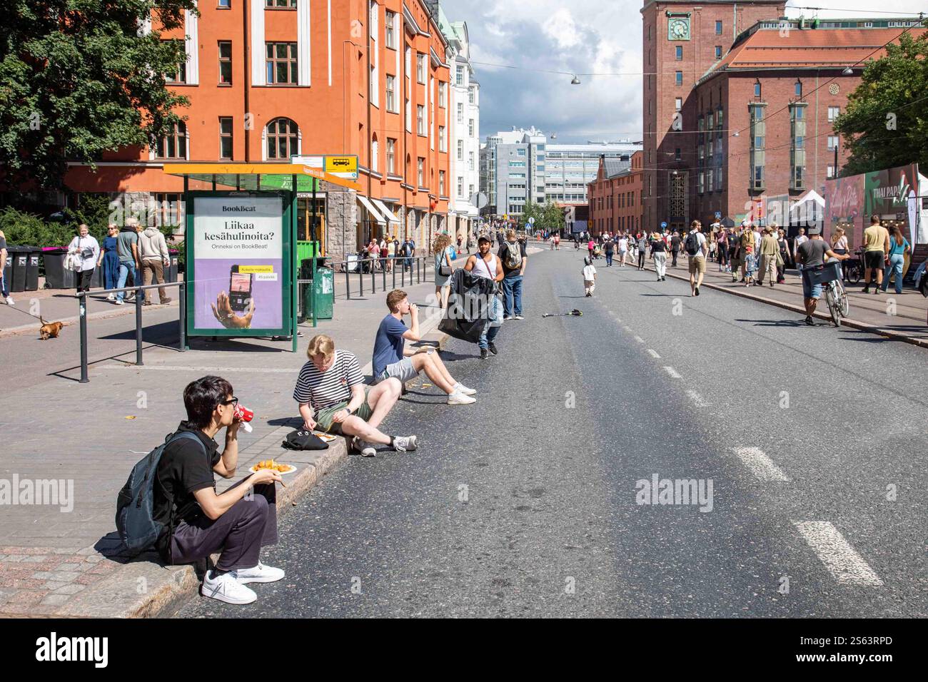 Des gens assis sur un trottoir mangeant de la nourriture de rue au Kallio Block Party 2024 à Helsinki, Finlande Banque D'Images