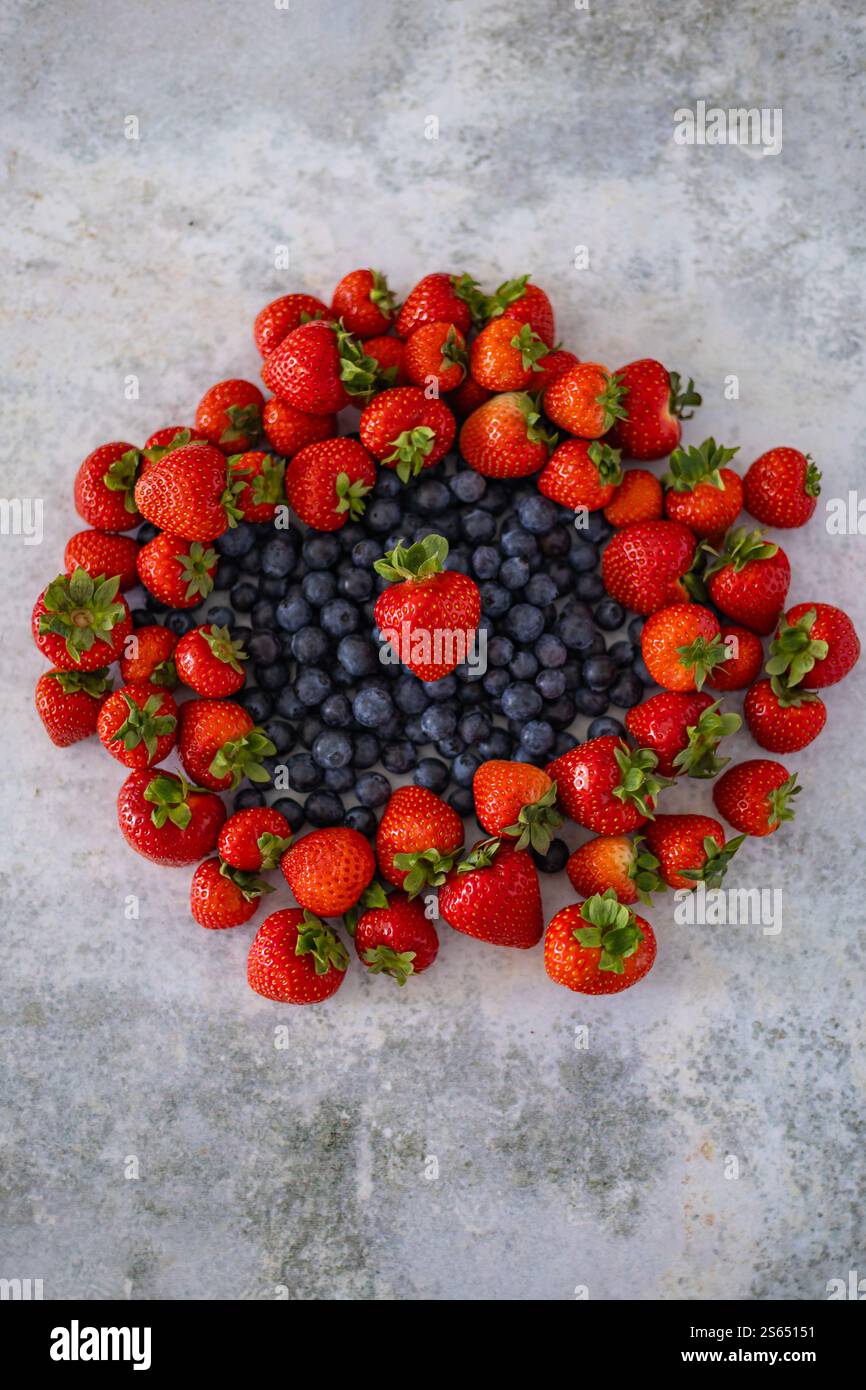 Composition verticale de fraises et de bleuets frais disposés dans un motif circulaire sur un fond gris rustique Banque D'Images