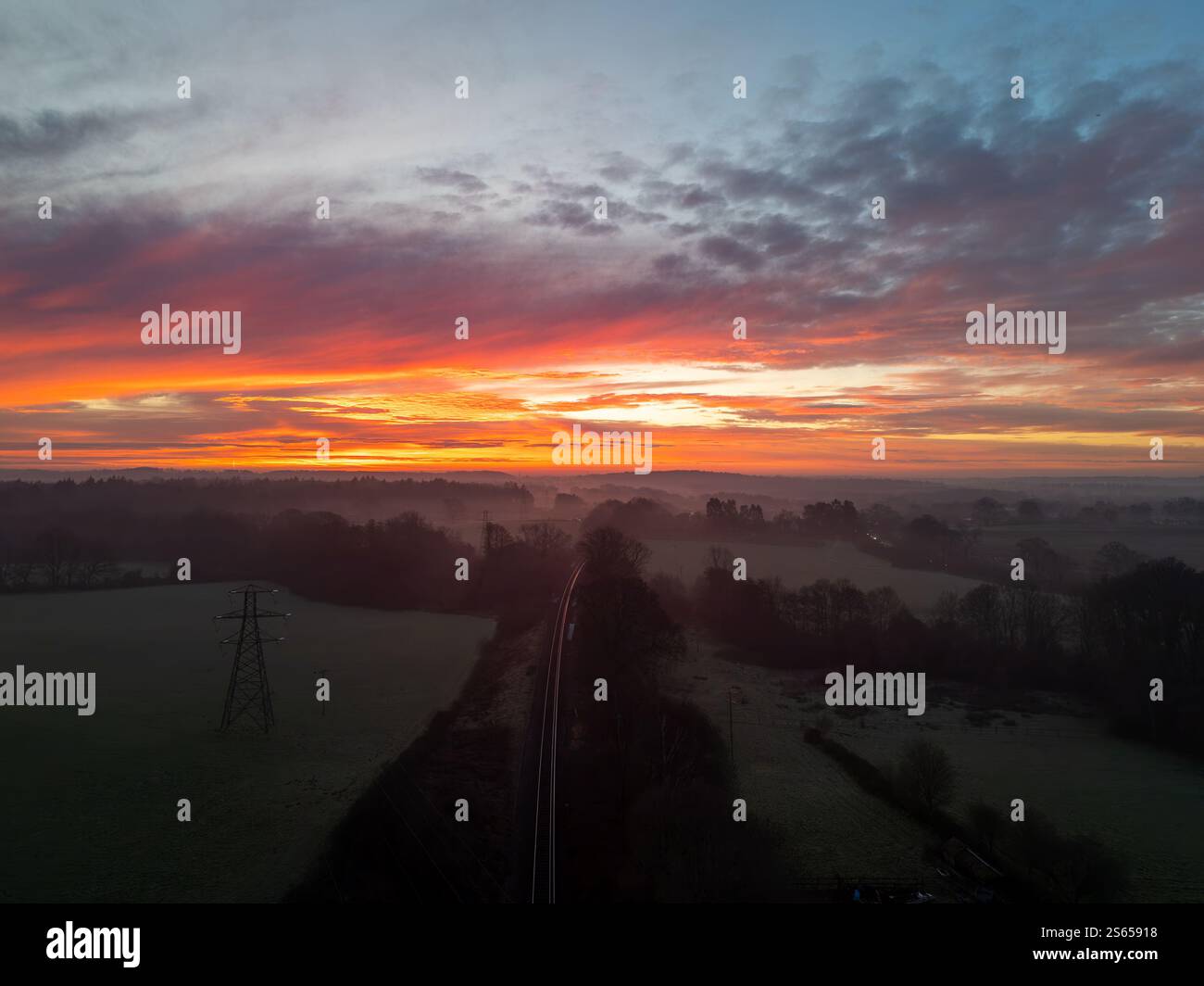 Vue aérienne d'un lever de soleil vibrant et coloré sur la campagne brumeuse près de Plymouth, Devon, avec une ligne de chemin de fer et un pylône d'électricité dans la for Banque D'Images