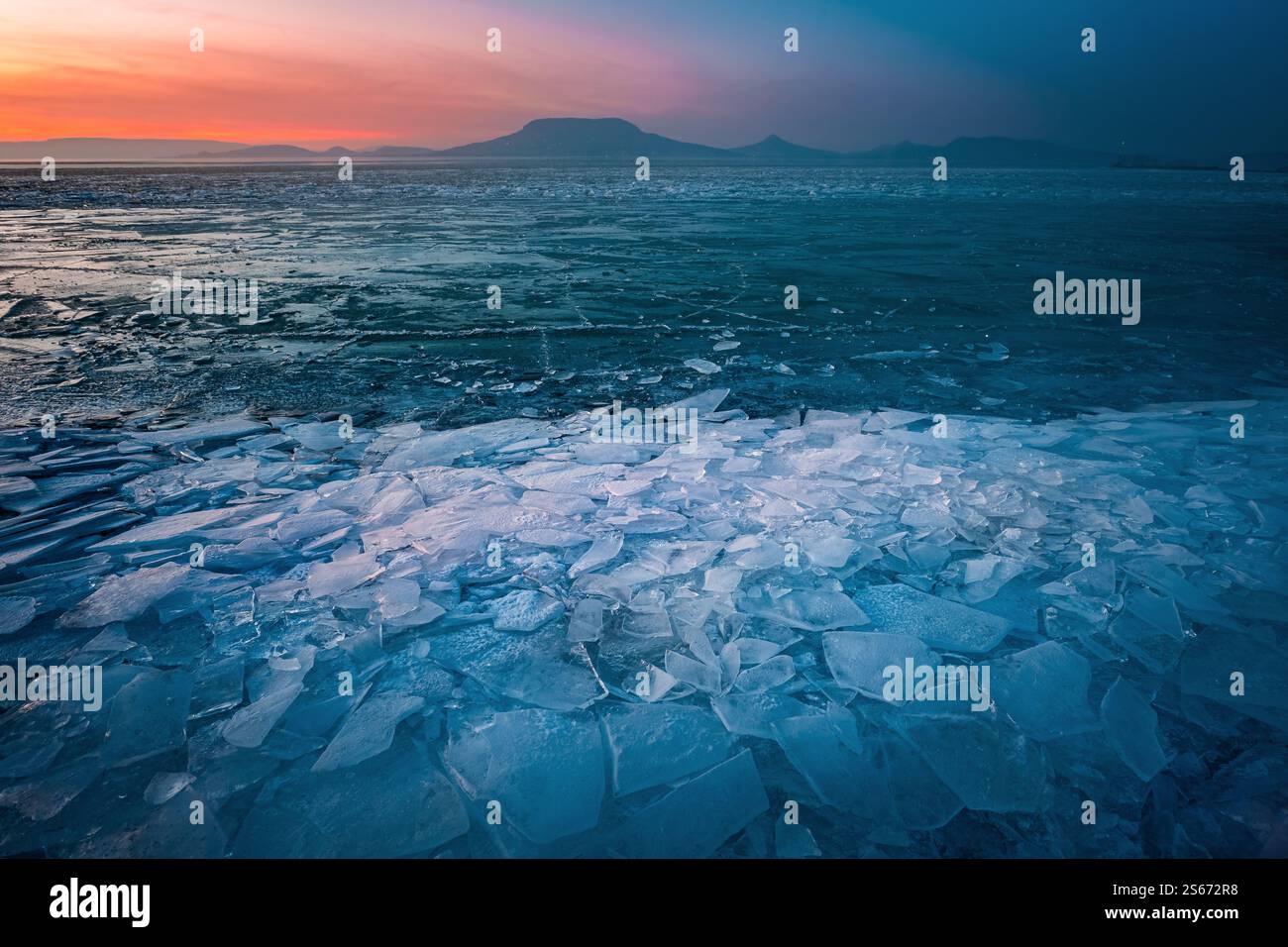 Fonyod, Hongrie - vue panoramique sur le lac Balaton gelé par un après-midi froid d'hiver avec glace brisée, ciel de coucher de soleil coloré doré et le mont Badacsony Banque D'Images
