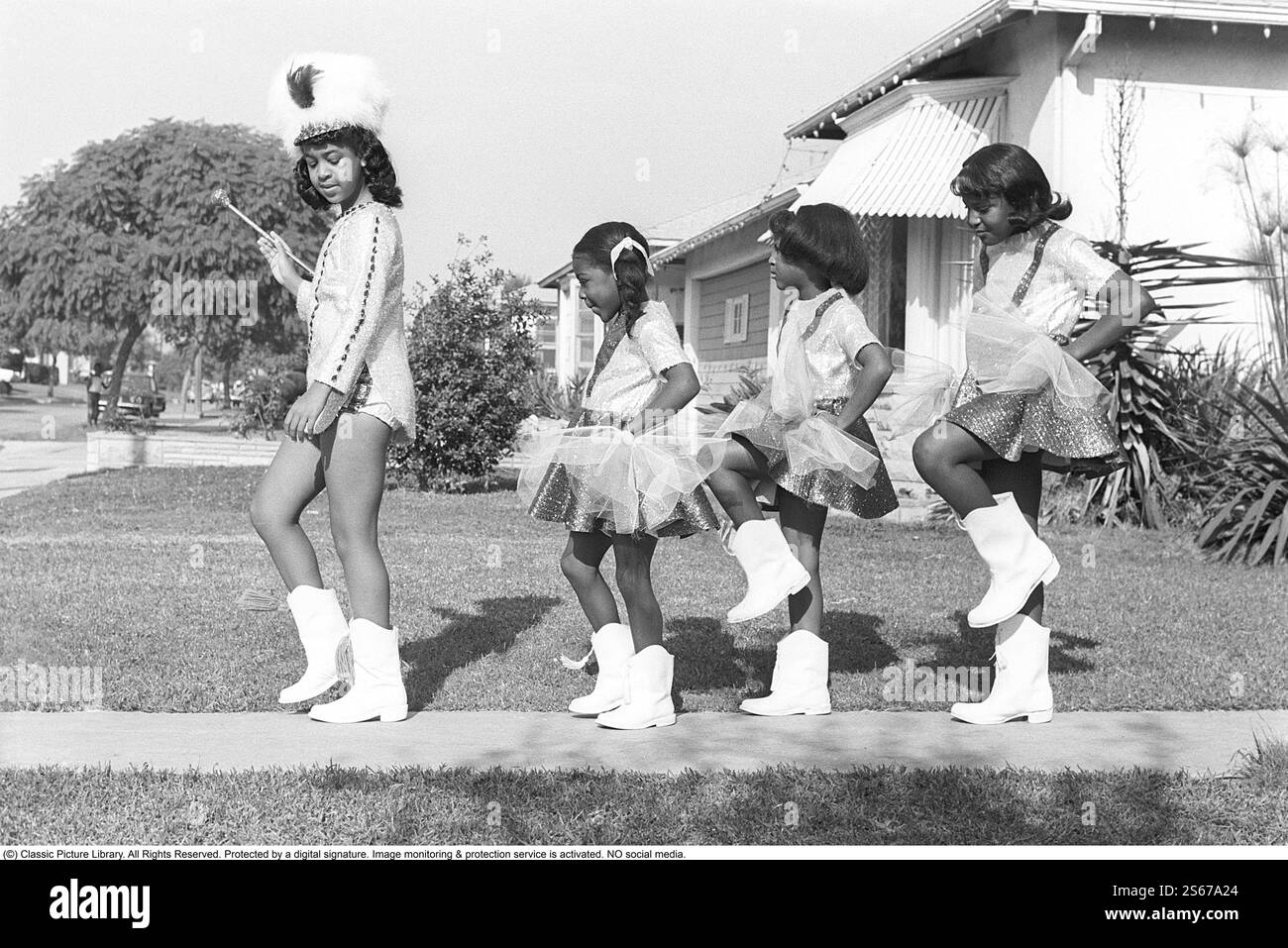 Pratiquer pour le grand défilé 1968. Quatre filles défilent devant le photographe vêtues de leurs uniformes. Une pratique qu'ils font sur l'allée d'une maison à Los Angeles avant le grand défilé. Les quatre filles portent des vêtements festifs et des bottes hautes blanches. Le plus ancien passe d'abord en tant que major de tambour portant la masse cérémonielle. USA 1968. Roland Palm réf. 15-5-20 Banque D'Images