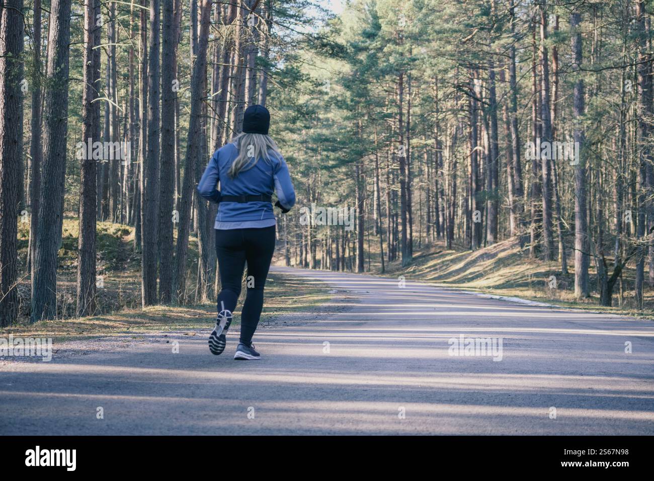 Une femme en vêtements de sport court le long d'un chemin forestier. Banque D'Images