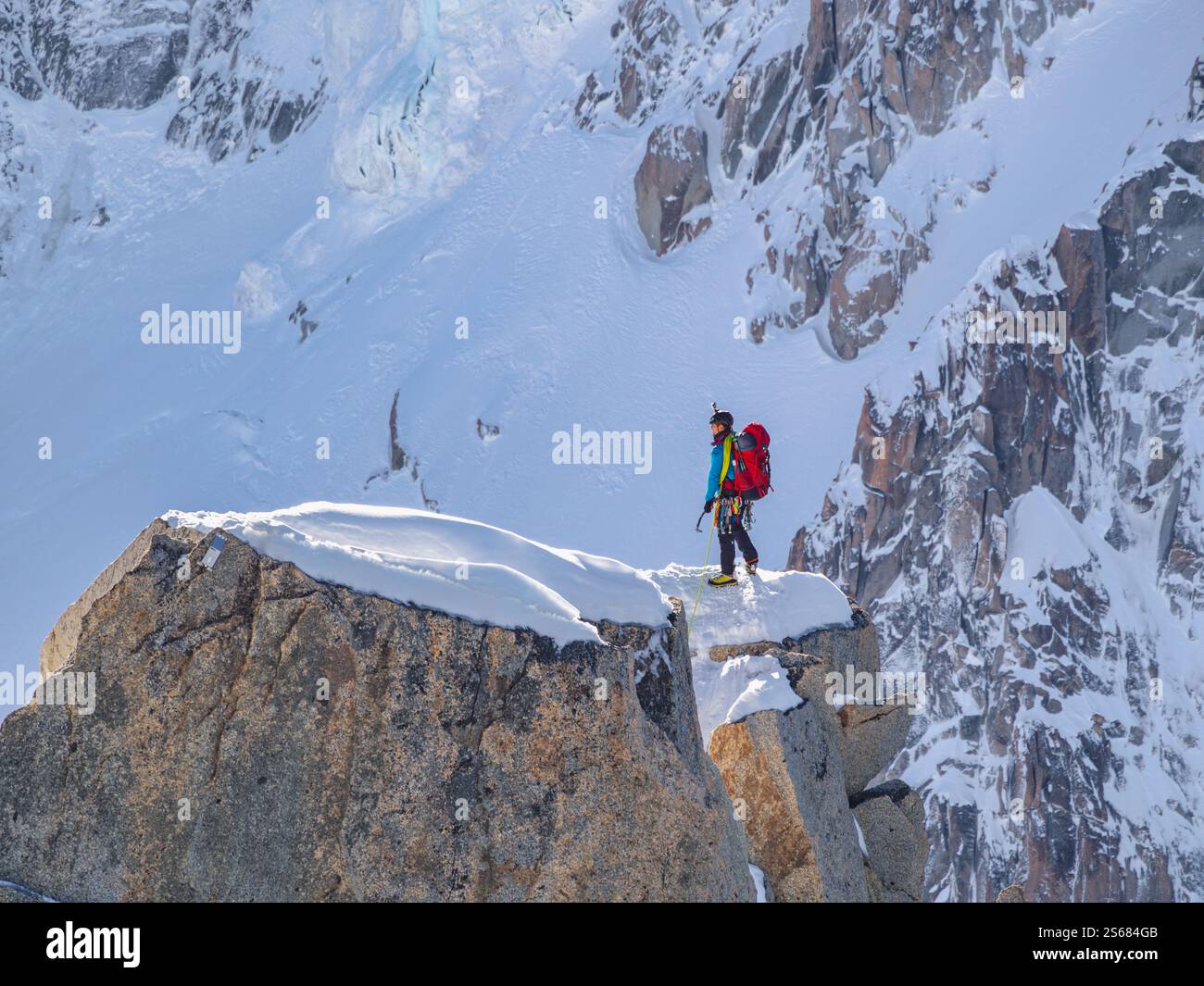 Un alpiniste, entièrement équipé d'un sac à dos rouge et d'un piolet, se dresse sur un bord rocheux enneigé près de l'aiguille du midi à Chamonix. Banque D'Images
