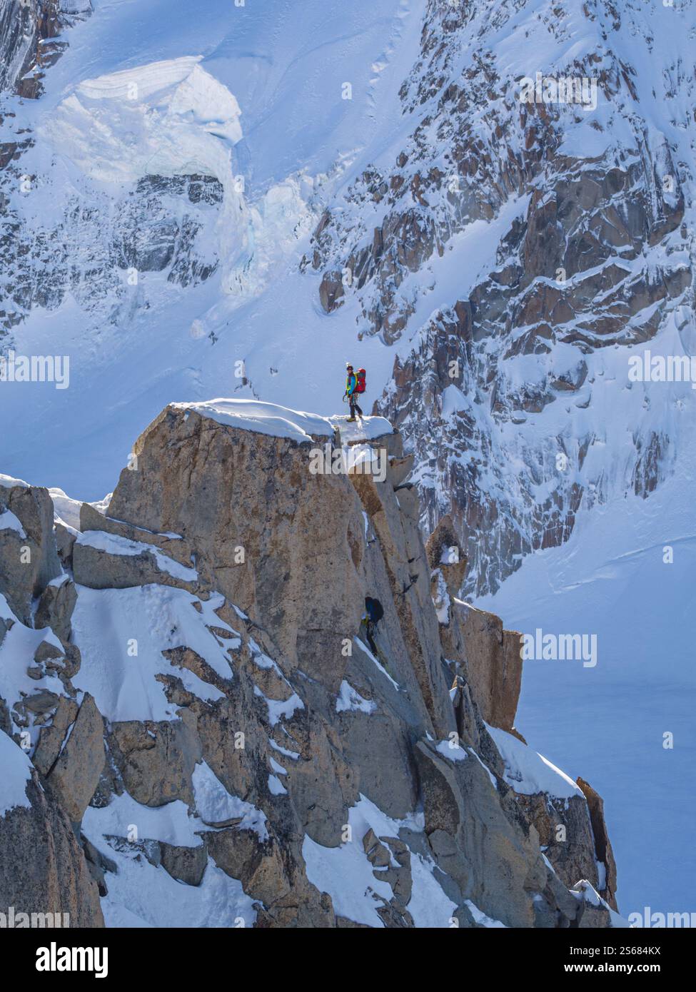 Un alpiniste, entièrement équipé d'un sac à dos rouge et d'un piolet, se dresse sur un bord rocheux enneigé près de l'aiguille du midi à Chamonix. Banque D'Images