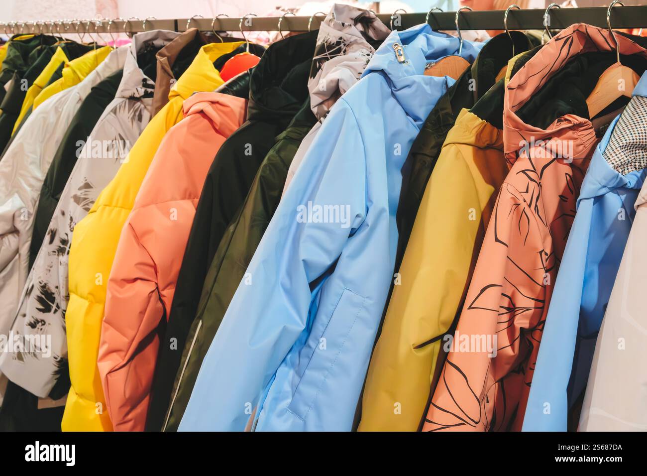 Un rack de vestes avec une jaune au milieu. Les vestes sont suspendues sur un rack, avec certaines d'entre elles étant vertes, bleues et roses Banque D'Images