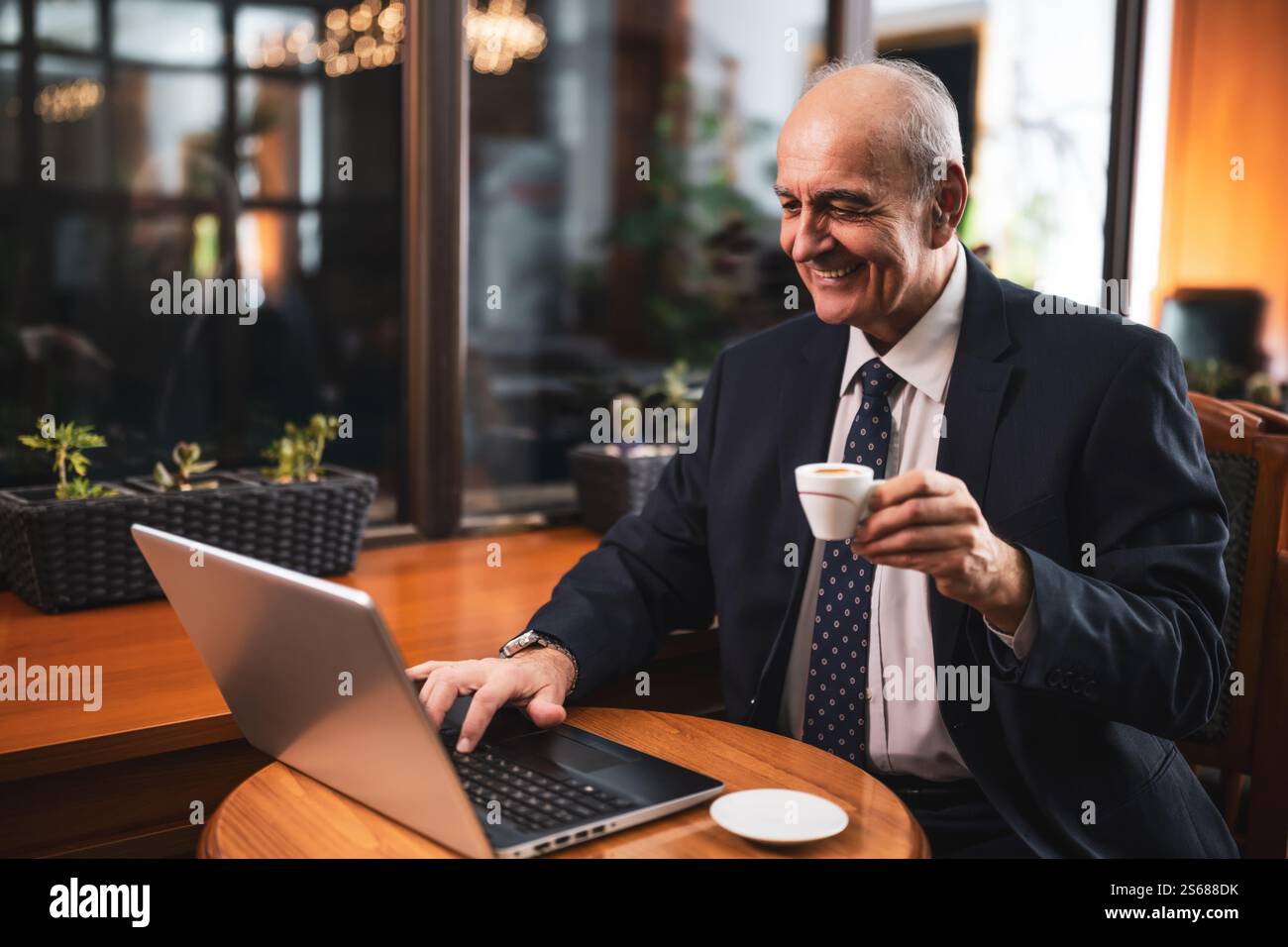 Homme d'affaires senior élégant travaillant sur ordinateur portable et buvant du café tout en étant assis dans le café de la ville. Banque D'Images