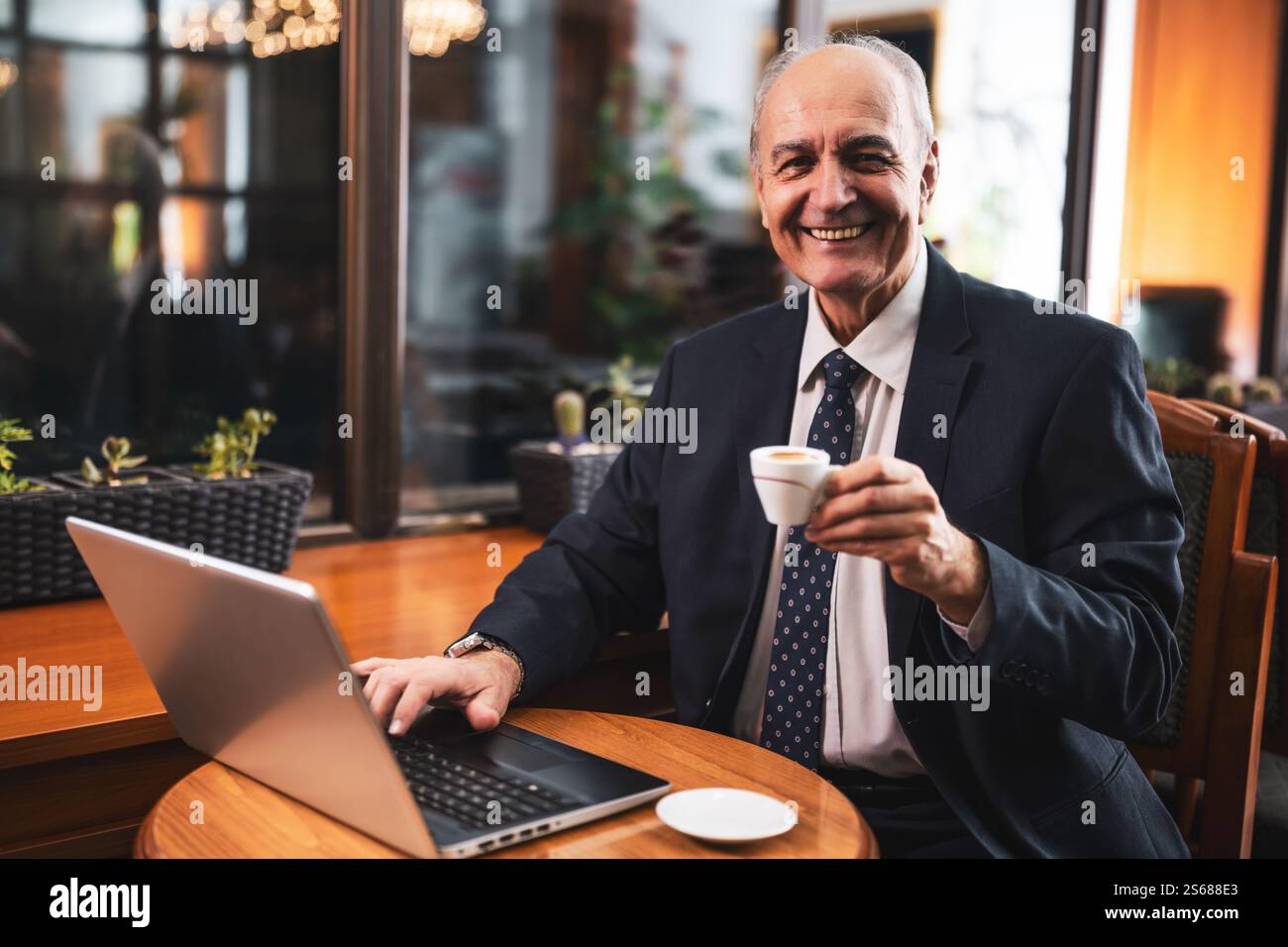 Homme d'affaires senior élégant travaillant sur ordinateur portable et buvant du café tout en étant assis dans le café de la ville. Banque D'Images