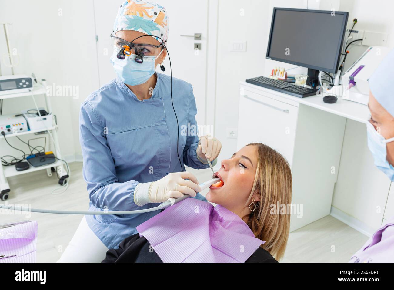 Femme dentiste portant une loupe examinant les dents d'un malade blond en clinique dentaire Banque D'Images